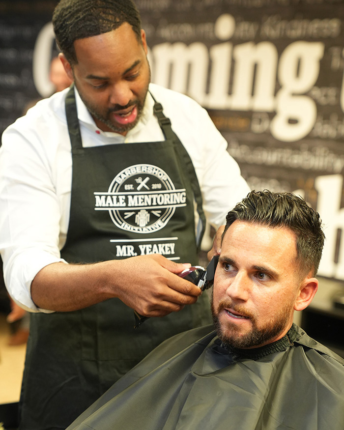 Fred Yeakey reminisces about all the haircuts he has provided throughout the years while giving a trim to Robert Bauscher, Eight Eleven Foundation Board Member